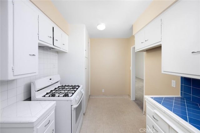 kitchen featuring tile countertops, tasteful backsplash, white gas range oven, and white cabinets