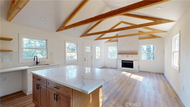 kitchen with a fireplace, backsplash, light wood-style floors, a sink, and light stone countertops