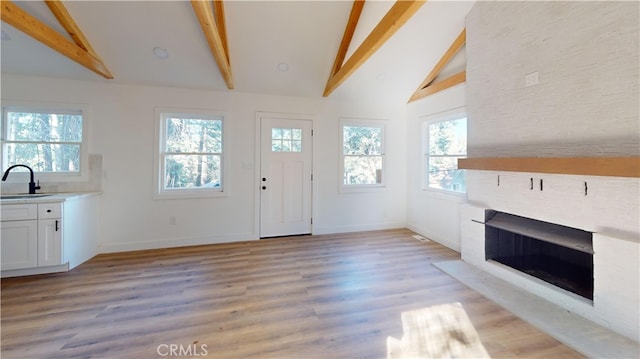 entrance foyer with vaulted ceiling with beams, a fireplace, light wood-style flooring, and baseboards