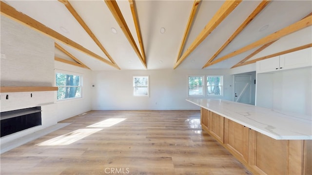 unfurnished living room with a wealth of natural light, a fireplace, and lofted ceiling with beams