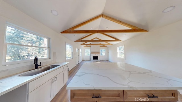 kitchen with lofted ceiling, a fireplace, a sink, open floor plan, and light stone countertops