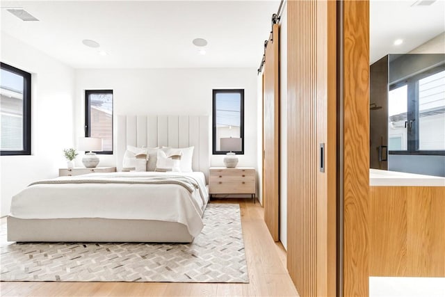 bedroom featuring light wood finished floors, multiple windows, a barn door, and recessed lighting