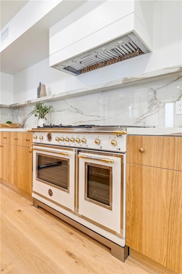 kitchen with light wood finished floors, premium range hood, range with two ovens, and modern cabinets