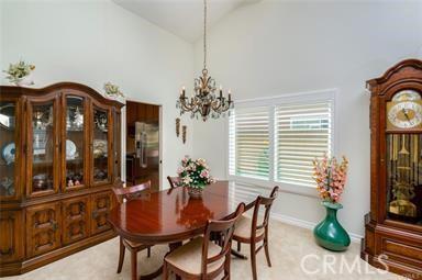 dining space with high vaulted ceiling, light carpet, a notable chandelier, and baseboards