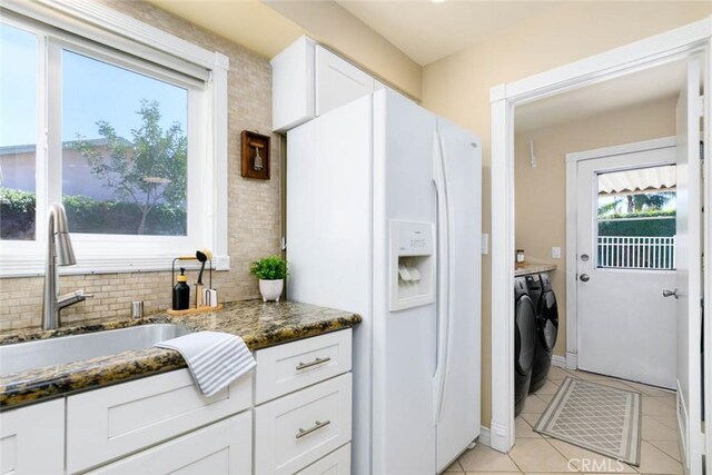 kitchen featuring white refrigerator with ice dispenser, white cabinetry, a sink, dark stone counters, and independent washer and dryer