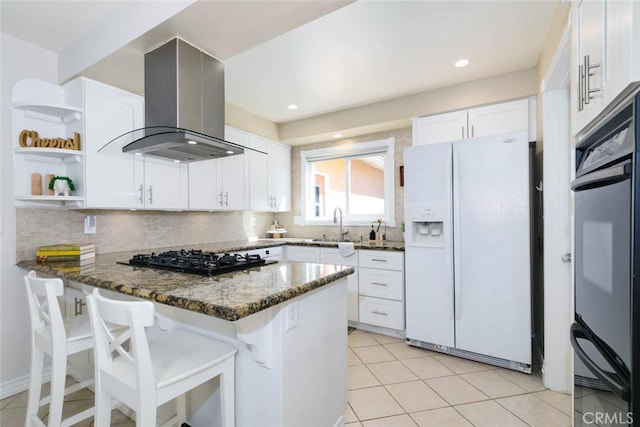 kitchen featuring dark stone countertops, a peninsula, black appliances, backsplash, and exhaust hood