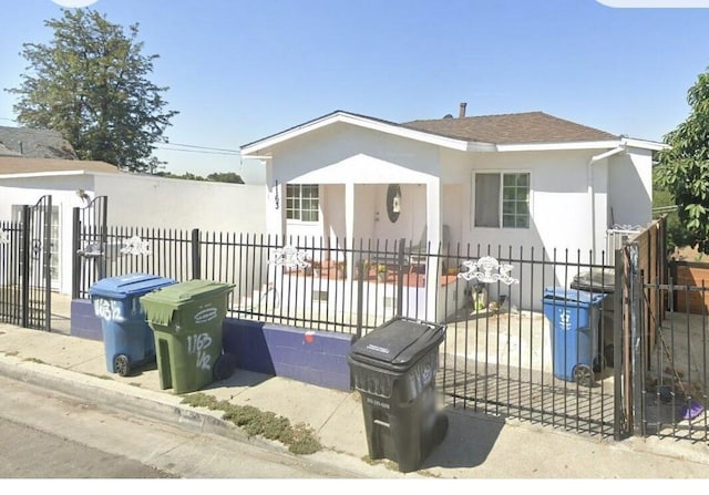 view of front facade featuring roof with shingles, a fenced front yard, a gate, and stucco siding