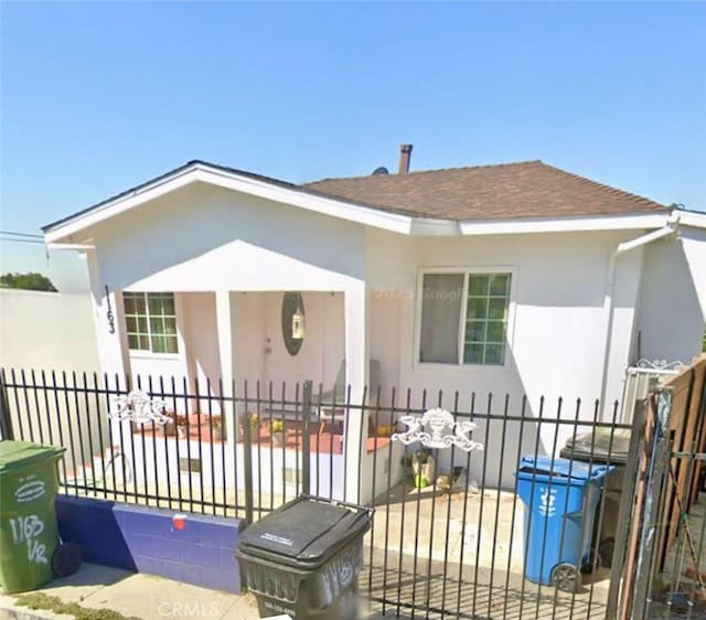 rear view of house featuring roof with shingles, a fenced front yard, and stucco siding