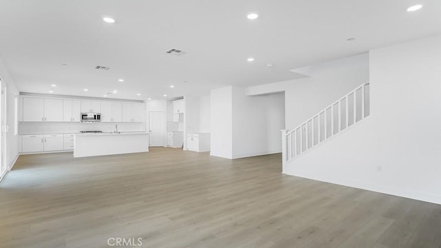 unfurnished living room featuring light wood finished floors, visible vents, recessed lighting, and stairs