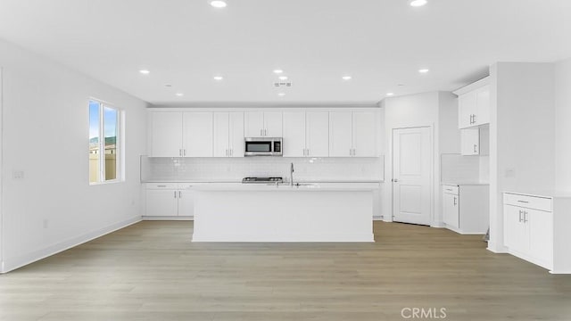 kitchen featuring stainless steel microwave, white cabinetry, light countertops, and light wood-style floors