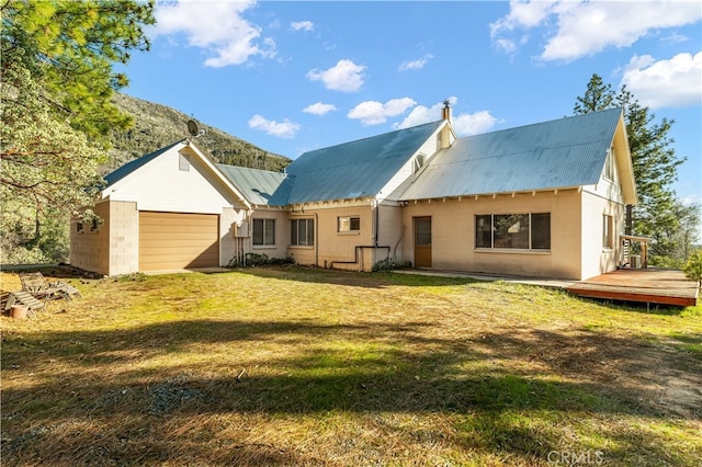 rear view of property featuring an attached garage, a wooden deck, metal roof, and a yard