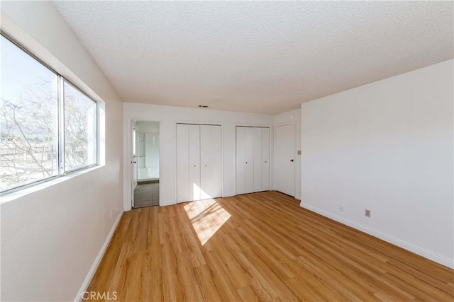 unfurnished bedroom with a textured ceiling, baseboards, two closets, and light wood-style floors