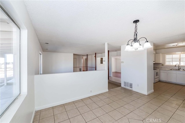 spare room with a textured ceiling, light tile patterned floors, a sink, visible vents, and baseboards