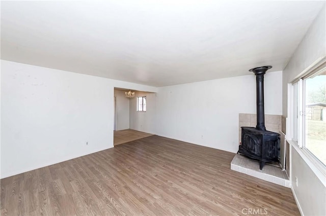 unfurnished living room with a wealth of natural light, wood finished floors, a wood stove, and a notable chandelier