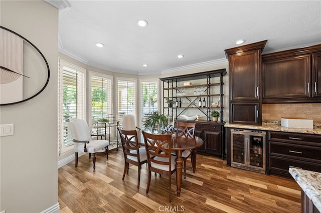 dining space with baseboards, wine cooler, ornamental molding, light wood-type flooring, and recessed lighting