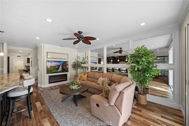 living area with ornamental molding, wood finished floors, a glass covered fireplace, and recessed lighting