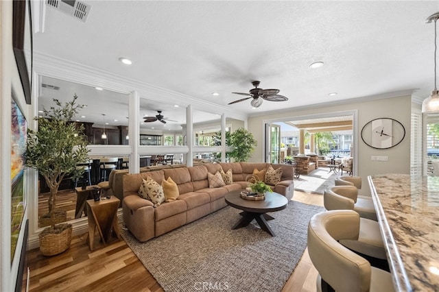 living room with crown molding, visible vents, and light wood-style floors