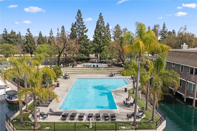 community pool featuring a water view, fence, and a patio