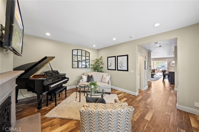 living room featuring baseboards, a fireplace with flush hearth, wood finished floors, and recessed lighting