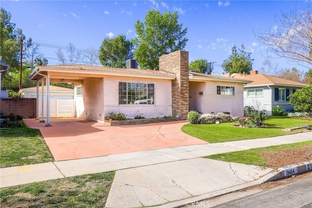 ranch-style home with concrete driveway, an attached carport, fence, a front lawn, and stucco siding