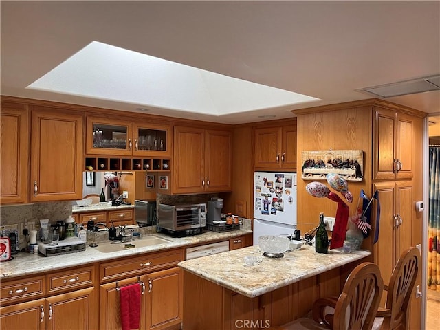 kitchen with a breakfast bar, white appliances, brown cabinetry, and a sink