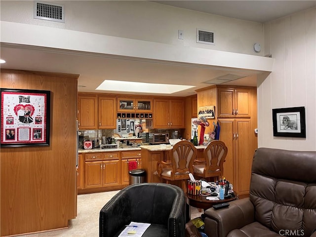 kitchen featuring open floor plan, glass insert cabinets, visible vents, and brown cabinets