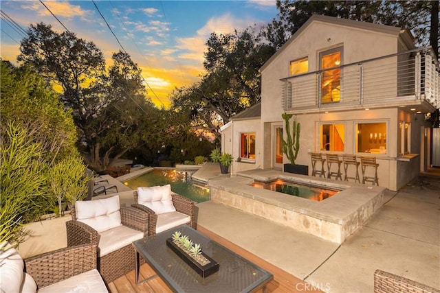 patio terrace at dusk featuring an outdoor pool, a balcony, a jacuzzi, outdoor dry bar, and outdoor lounge area