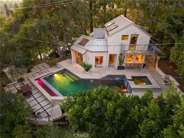 rear view of property with a balcony, an in ground hot tub, stairs, stucco siding, and a patio area