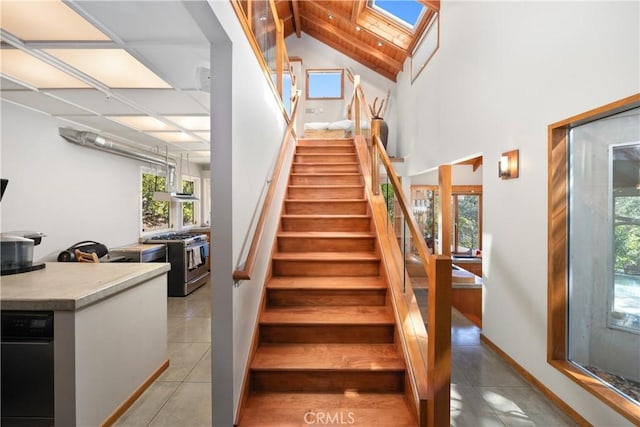 staircase with high vaulted ceiling, a skylight, tile patterned flooring, and baseboards