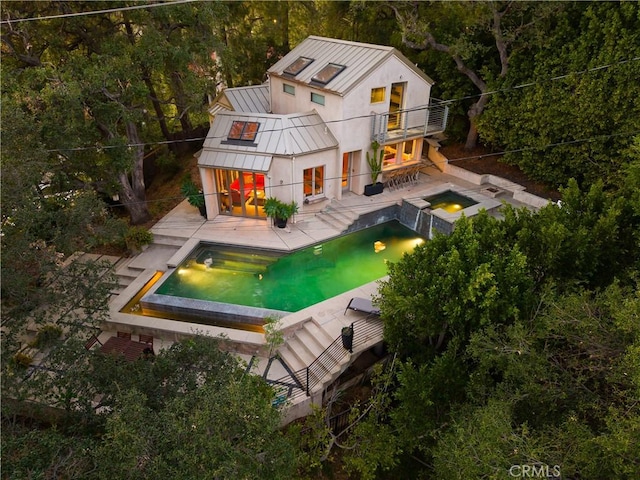 rear view of house with metal roof, a balcony, an in ground hot tub, a standing seam roof, and a patio area