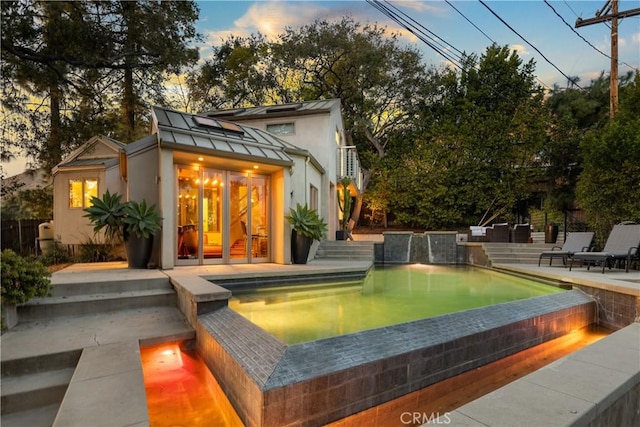 pool at dusk featuring an infinity pool and a patio area