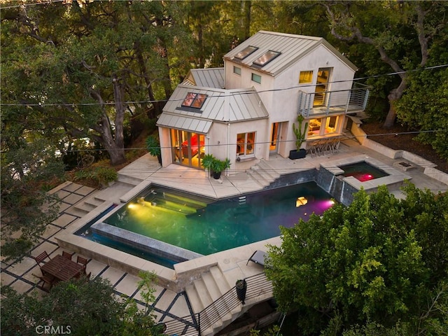 rear view of property with metal roof, a balcony, an in ground hot tub, a standing seam roof, and a patio area