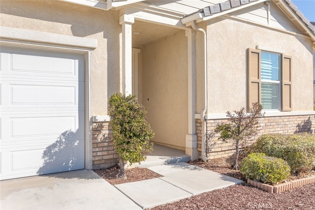 view of exterior entry featuring a garage, stone siding, and stucco siding