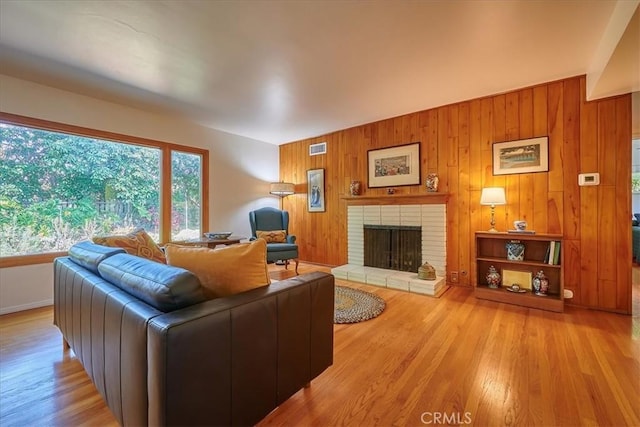 living area featuring a brick fireplace, visible vents, wooden walls, and wood finished floors