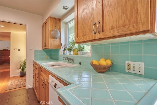 kitchen with tile countertops, white dishwasher, a sink, decorative backsplash, and tile patterned floors