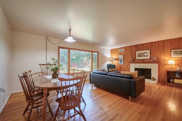 dining area featuring light wood-style floors, wooden walls, a fireplace, and visible vents