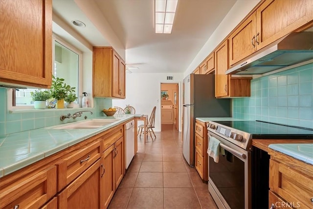 kitchen featuring dishwasher, tile countertops, stainless steel range with electric cooktop, under cabinet range hood, and a sink