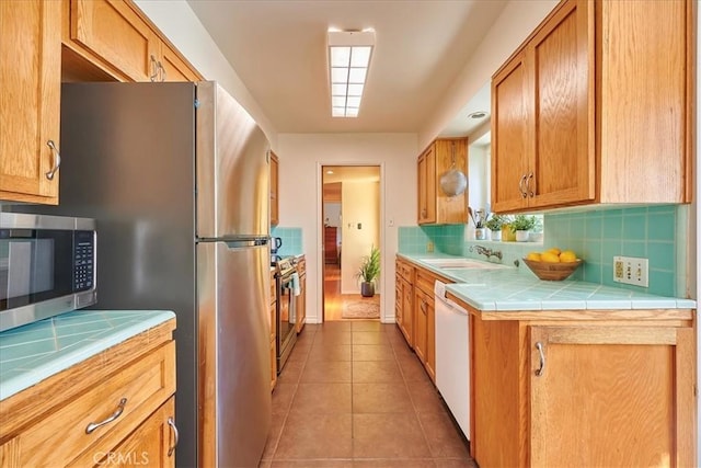 kitchen featuring light tile patterned floors, a sink, appliances with stainless steel finishes, backsplash, and tile counters