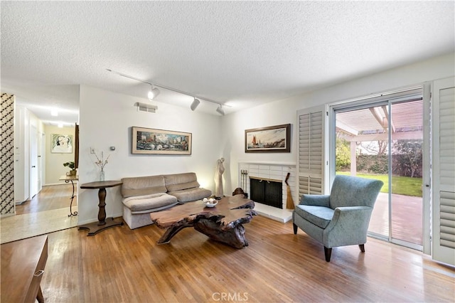 living room featuring a textured ceiling, a fireplace, wood finished floors, and visible vents