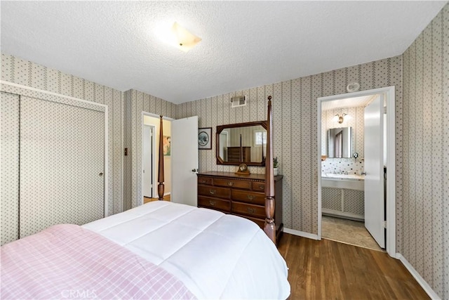 bedroom featuring wallpapered walls, baseboards, visible vents, wood finished floors, and a textured ceiling