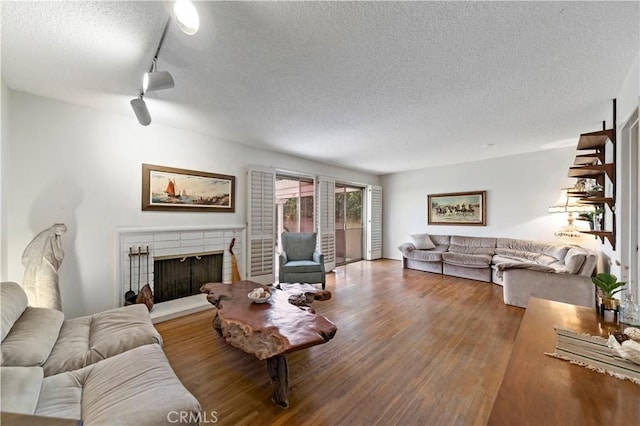 living room with a textured ceiling, a tiled fireplace, wood finished floors, and track lighting