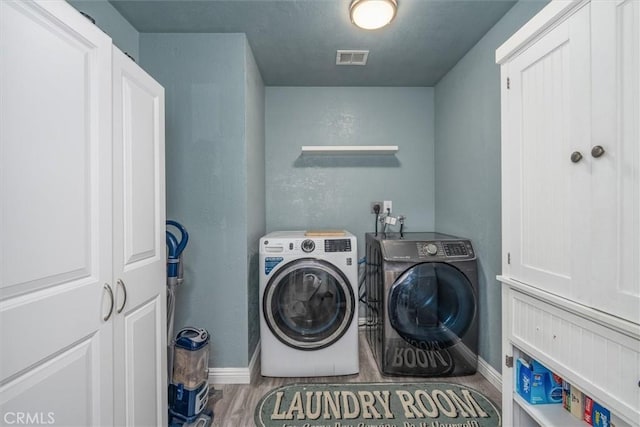 clothes washing area featuring laundry area, visible vents, baseboards, wood finished floors, and washing machine and dryer