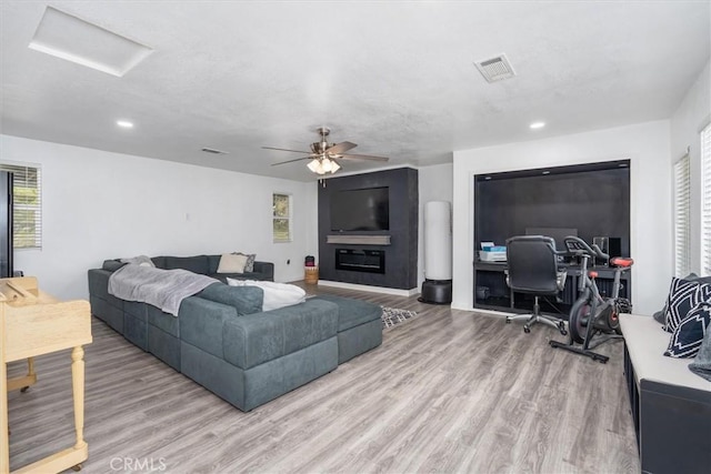 living room with a ceiling fan, a glass covered fireplace, visible vents, and wood finished floors