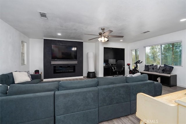 living area with light wood finished floors, a fireplace, visible vents, and a ceiling fan