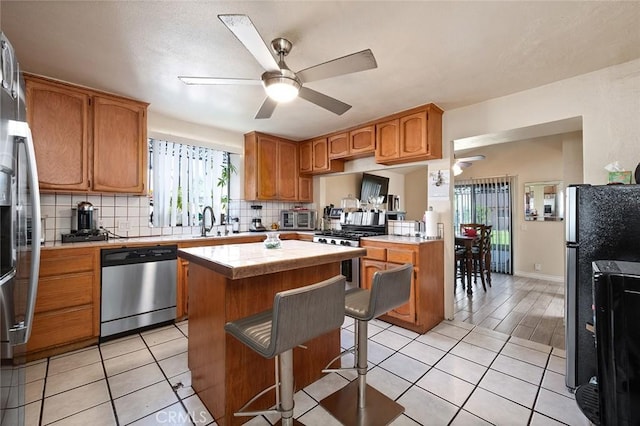 kitchen featuring appliances with stainless steel finishes, a sink, a ceiling fan, and decorative backsplash