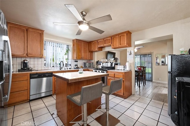 27447 Cypress St, Highland, CA 92346 - kitchen with appliances with stainless steel finishes, a ceiling fan, tasteful backsplash, a kitchen island, and a kitchen bar