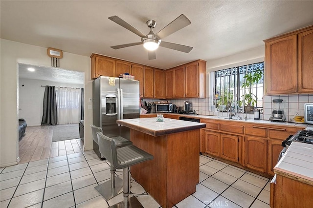 kitchen featuring a center island, tile countertops, decorative backsplash, appliances with stainless steel finishes, and light tile patterned flooring