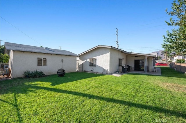 back of property featuring ceiling fan, stucco siding, fence, and a lawn