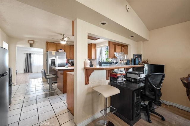 kitchen with a breakfast bar, stainless steel refrigerator with ice dispenser, backsplash, brown cabinetry, and a peninsula