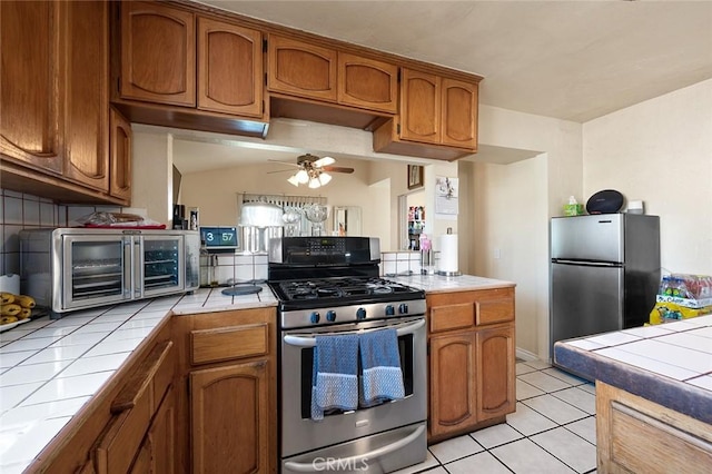 27447 Cypress St, Highland, CA 92346 - kitchen featuring appliances with stainless steel finishes, tile counters, brown cabinetry, and ceiling fan